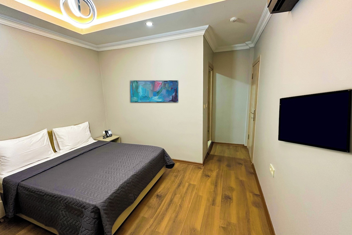 A hotel room with a bed, a painting, a phone on the nightstand, and a TV mounted on the wall.