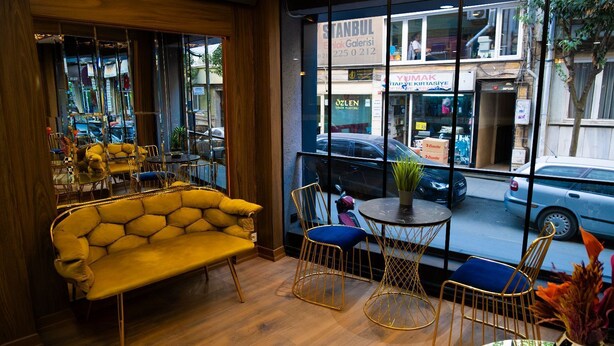 A cozy seating area with a yellow sofa and a small round table, large windows with a view of the street, and a wooden floor.