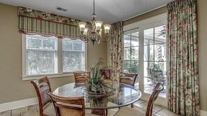 A dining area with a round glass table, wooden chairs, a chandelier, and floral curtains. - Unwind & Relax 3 Bedroom Home Near the Beach (North Myrtle Beach)