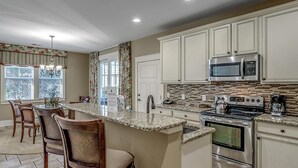 A modern kitchen with a central island, stainless steel appliances, and a dining area with wooden chairs. - Unwind & Relax 3 Bedroom Home Near the Beach (North Myrtle Beach)