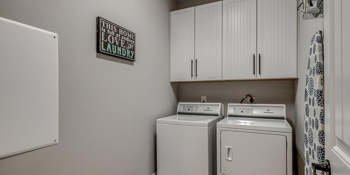 A laundry room with two white washing machines, a white refrigerator, and a wall-mounted sign.