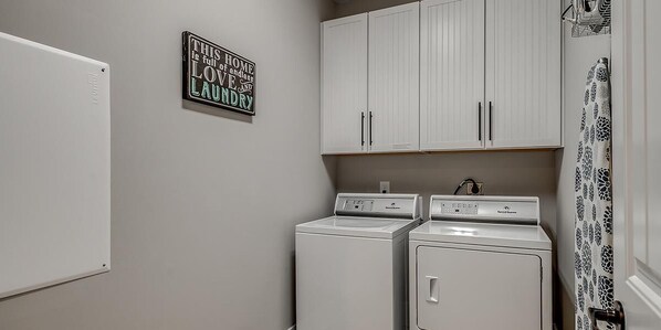 A laundry room with two white washing machines, a white refrigerator, and a wall-mounted sign.