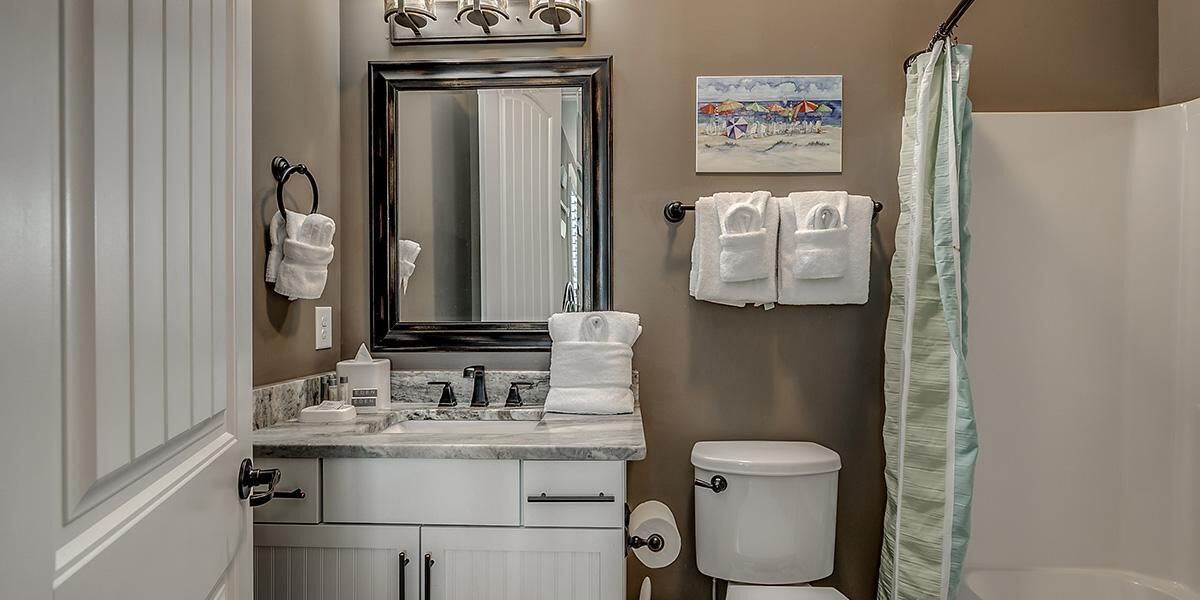 A bathroom with a sink, mirror, towel rack, toilet, and shower curtain.