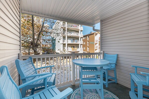 A balcony with blue chairs and a table, overlooking a building with balconies.
