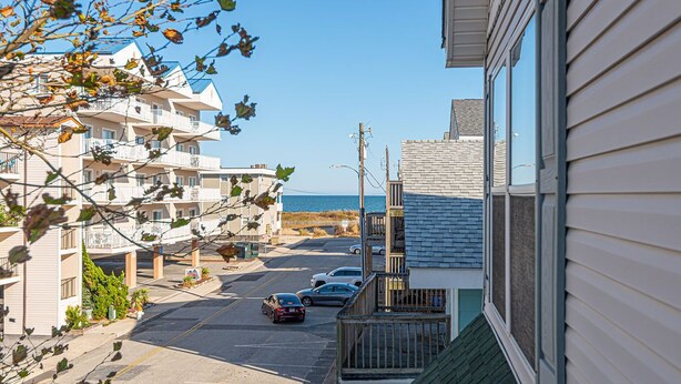 En bostadsgata vid kusten med flerfamiljshus, fri utsikt över havet och parkerade bilar.