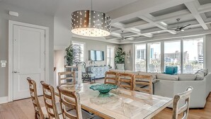 A spacious living area with a dining table, chairs, a sofa, and a large window offering a city view.