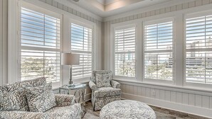A room with large windows, a chair, a table, and a lamp.