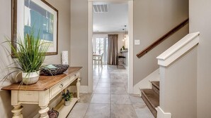 A hallway with a wooden console table, a potted plant, and a framed picture. A staircase with a white railing leads to another room. - Discover Serenity and Elegance in This 3BR/3.5BA (North Myrtle Beach)