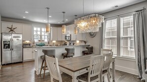 A modern kitchen with a central island, bar stools, pendant lighting, and a starfish decoration on the refrigerator. - Unparalleled Luxury 4 Bdrm Home with Amenities (North Myrtle Beach)