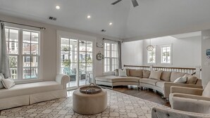 A spacious living room with a large sectional sofa, a round ottoman, and a dining area with a table and chairs. - Unparalleled Luxury 4 Bdrm Home with Amenities (North Myrtle Beach)