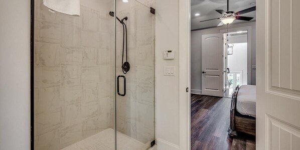 A glass-enclosed shower with a control panel, a ceiling fan, and a wooden floor.