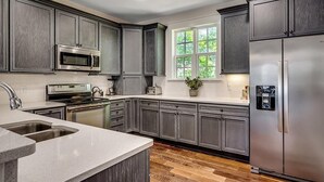 A modern kitchen with dark cabinetry, stainless steel appliances, a large window, and a built-in water dispenser.