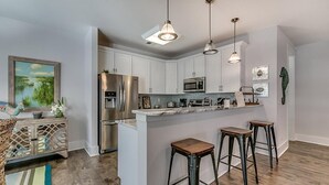 A modern kitchen with white cabinetry, stainless steel appliances, and a central island with stools. - Coastal Dream: 4 Bdrm Vacation Home with Pool (North Myrtle Beach)