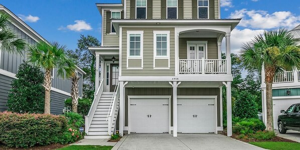 A two-story house with a balcony, two garage doors, and a staircase leading to the entrance.