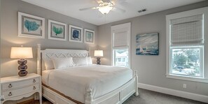 A bedroom with a bed, two bedside tables, a ceiling fan, and artwork on the walls.