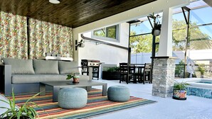 A modern outdoor living area with a sofa, ottomans, a striped rug, and a barbecue grill. - Orlando Vacation Rental Heated Pool & Spa 5 BR 3 BA Near Space, Nature, Disney  (Titusville)