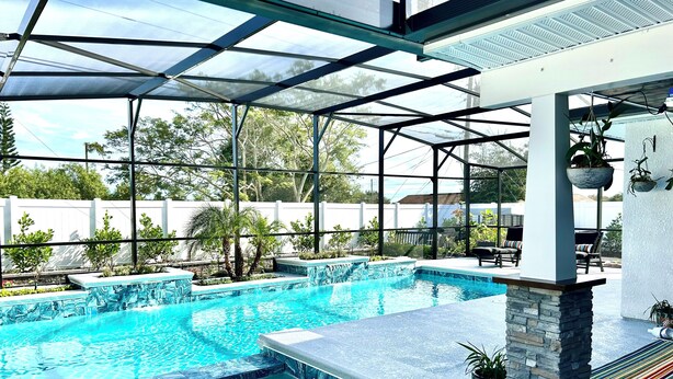 A swimming pool with a glass enclosure, stone pillars, and outdoor furniture. - Orlando Vacation Rental Heated Pool & Spa 5 BR 3 BA Near Space, Nature, Disney  (Titusville)