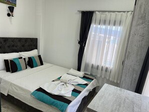 A neatly made bed with a striped bedspread and pillows, a bedside table, and a window with sheer curtains. - Tiana Butik Otel (Bodrum)