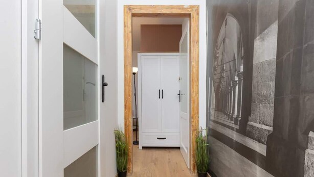 Un pasillo con una puerta blanca, piso de madera y un mural en la pared.