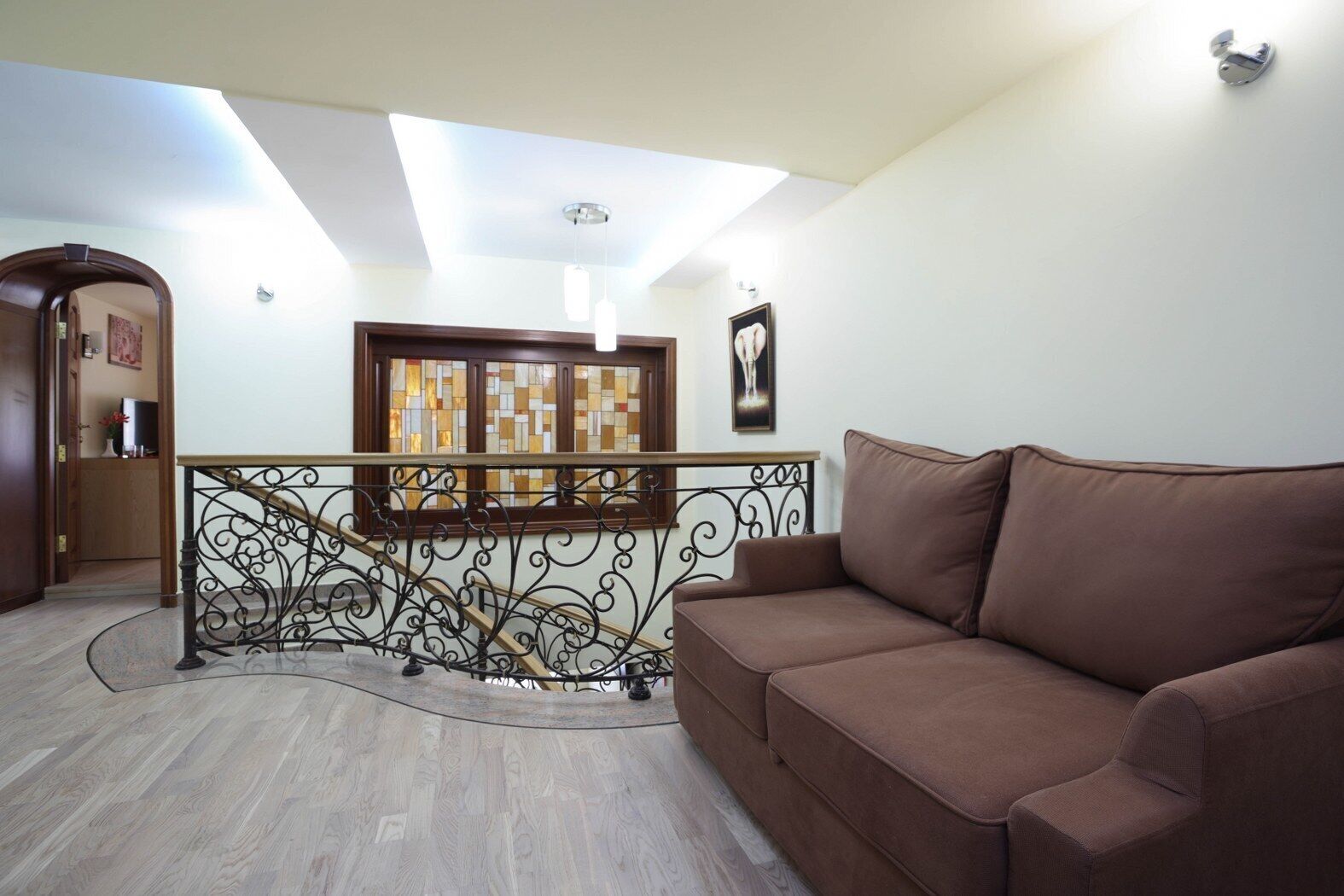 A spacious living area with a brown sofa, a wooden staircase with a wrought iron railing, and a stained glass window.