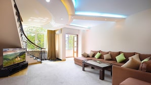 Un salon moderne avec un canapé, une table basse et un téléviseur. On y trouve un escalier avec une rampe et une vue sur la verdure à l’extérieur.