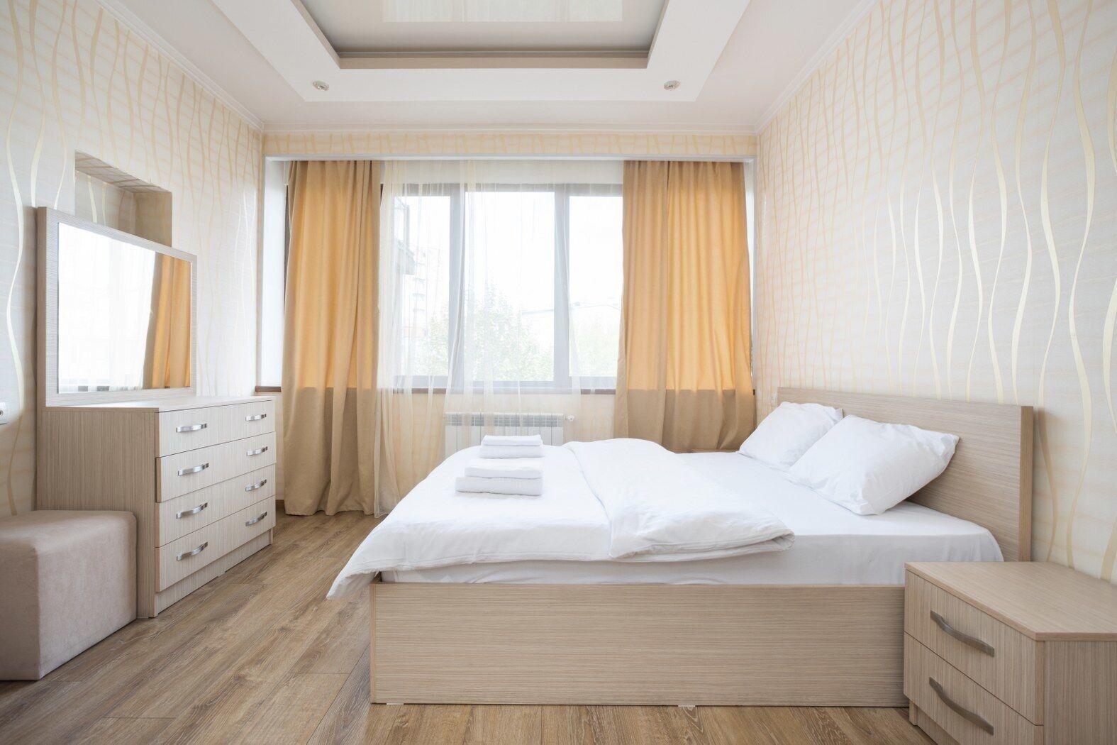 A modern bedroom with a wooden bed, a bedside table, a dresser, and a mirror.
