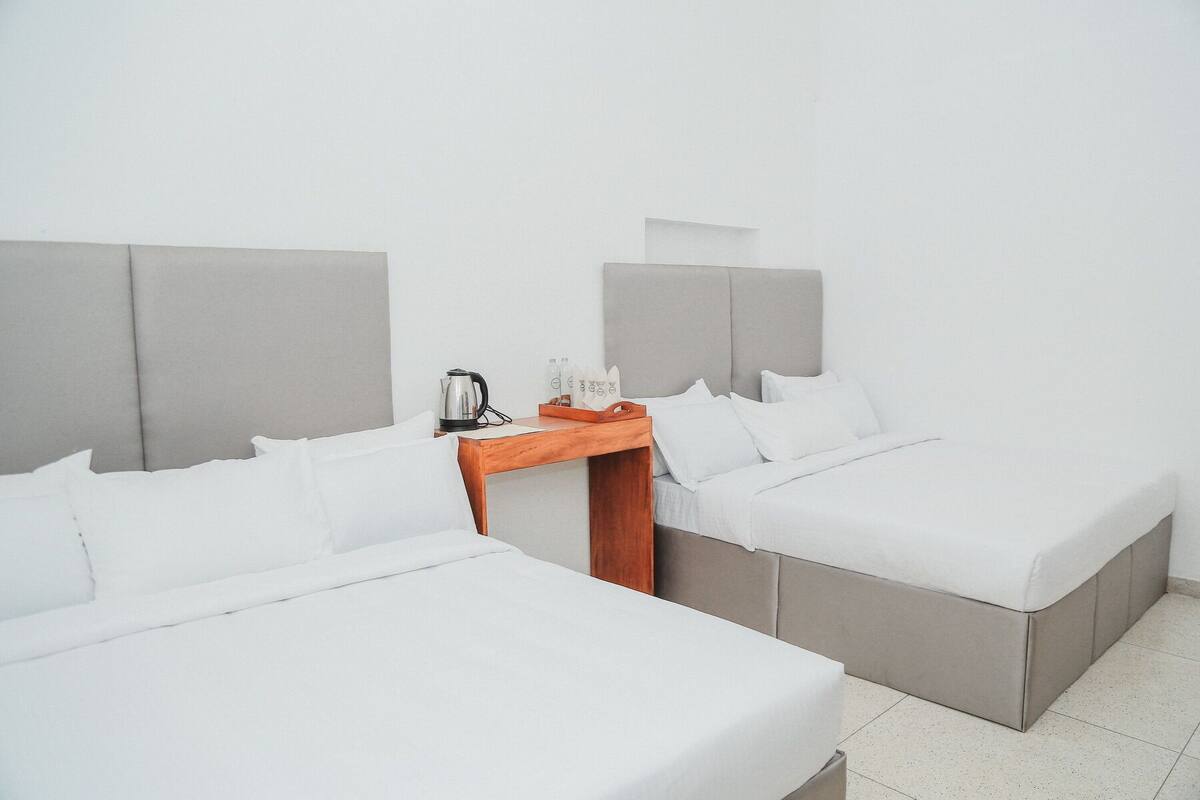 A hotel room with two beds, a wooden nightstand, a kettle, and a tray with toiletries.