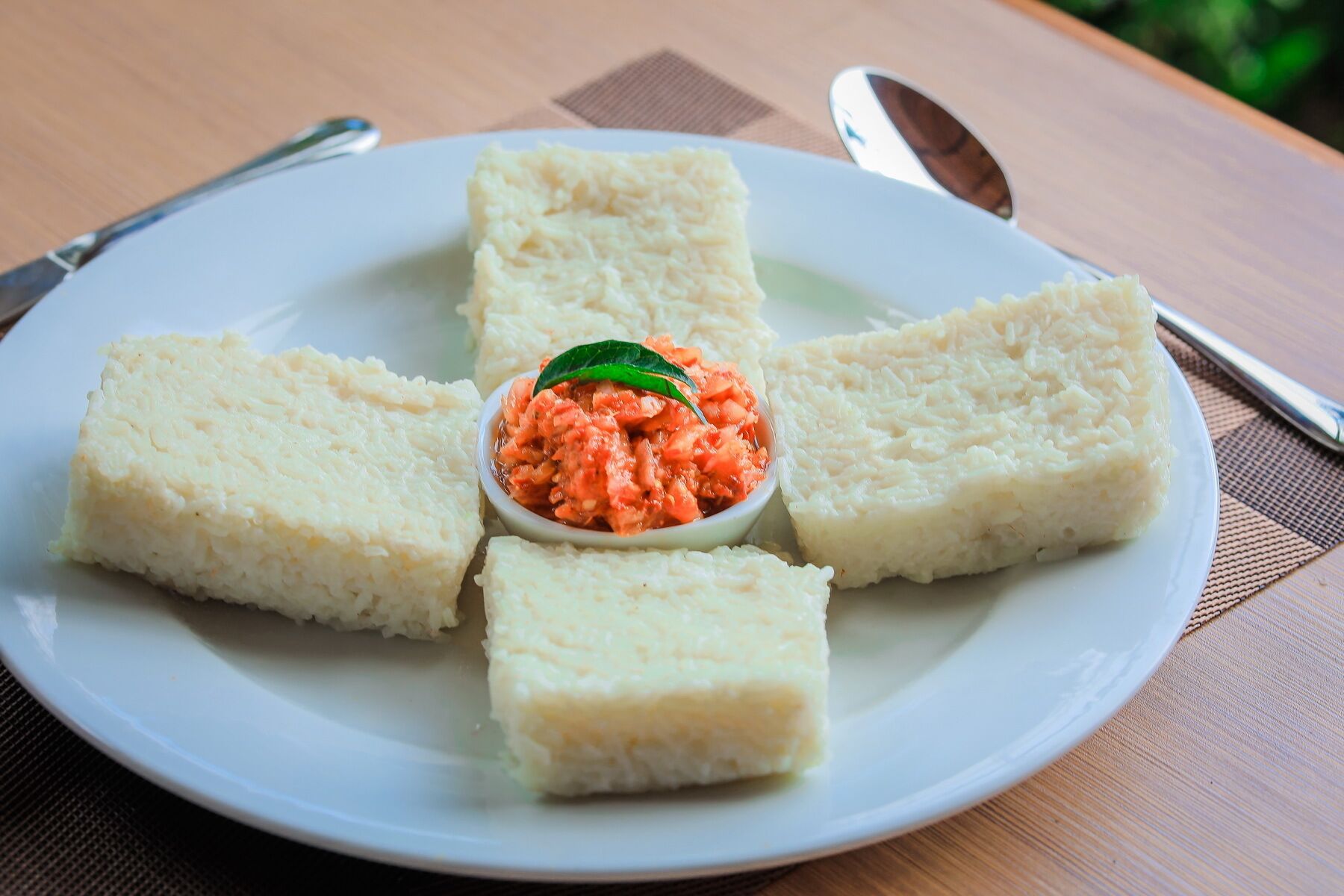 A plate with four pieces of white food and a small bowl of red sauce in the center.