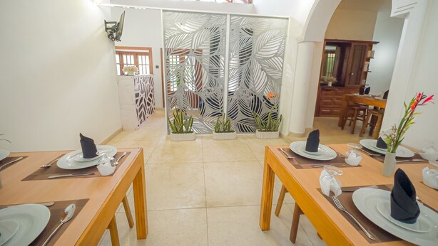 Un comedor con mesas y sillas de madera, platos blancos y un separador decorativo con hojas de palma.