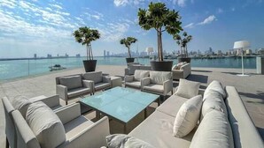 Un lounge en la azotea con asientos al aire libre, plantas en macetas grandes y vistas del horizonte de la ciudad y del agua.