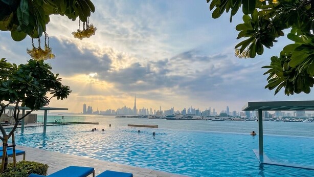 Una piscina con sillones de descanso, vista al horizonte de la ciudad y una masa de agua.