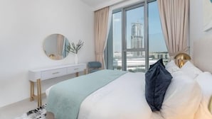 Une chambre moderne avec un grand lit, une commode blanche, un miroir rond et une vue sur le paysage urbain, visible à travers une grande fenêtre.