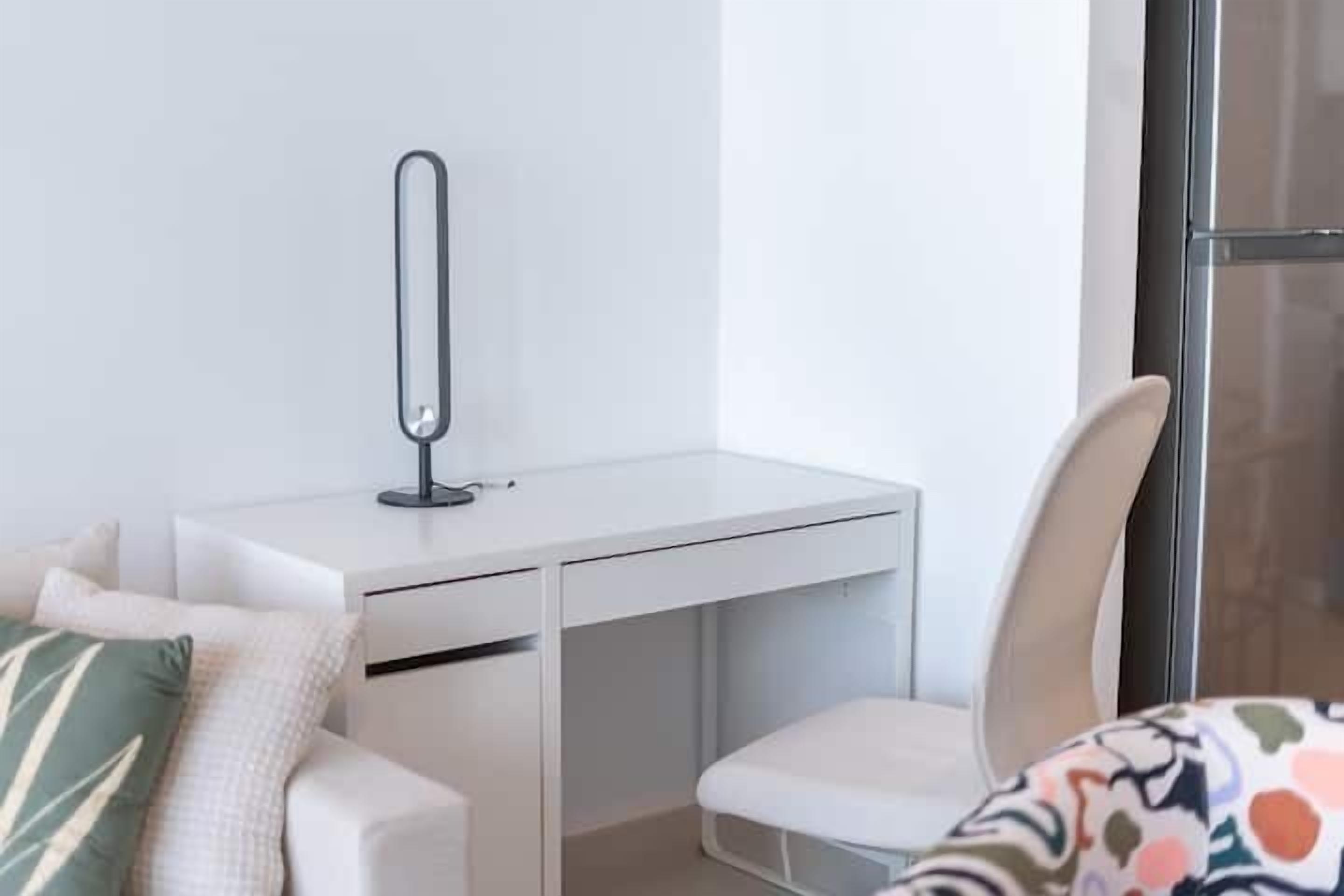 Habitació moderna i minimalista amb escriptori blanc, una cadira i un finestral gran.