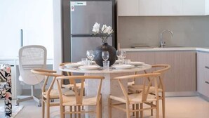 Una mesa redonda de comedor con seis sillas de madera, un florero con flores blancas y una cocina moderna al fondo.