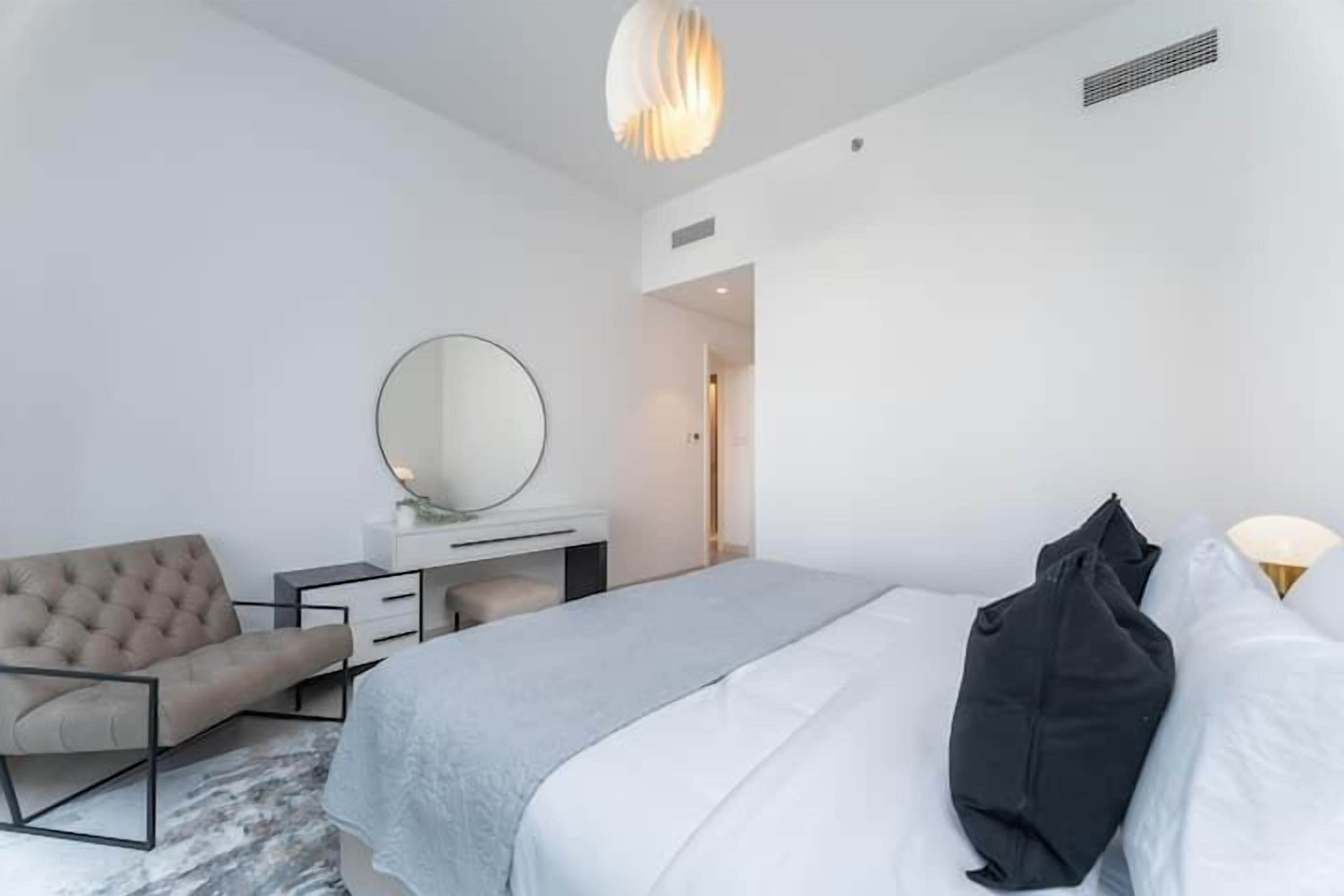 A modern hotel room with a bed, a seating area, a desk, and a large mirror.