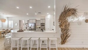 A modern kitchen with white cabinetry, a central island with bar stools, and a neon sign on the wall. - Lux 5BR Villa w Pool, Spa, RV Parking, Sleeps 12 (Henderson)