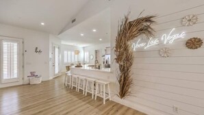 A modern kitchen with white cabinetry, a bar area with stools, and a neon sign on the wall. - Lux 5BR Villa w Pool, Spa, RV Parking, Sleeps 12 (Henderson)