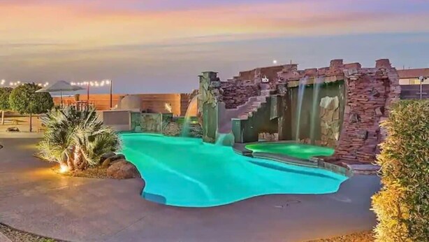 A swimming pool with a waterfall feature, surrounded by stone structures and palm trees. - Lux 5BR Villa w Pool, Spa, RV Parking, Sleeps 12 (Henderson)
