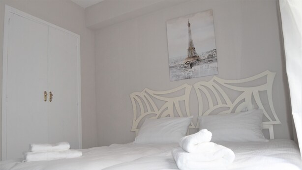 Un lit bien fait, avec du linge de lit et des serviettes blanches, une tête de lit blanche et une image de la Tour Eiffel accrochée au mur.