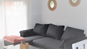 Un salon moderne avec un canapé gris, une petite table sur laquelle se trouve un panier, et deux miroirs fixés au mur.