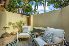 A patio area with wicker furniture and a cushioned sofa, surrounded by palm trees and a clear sky. - Maui Kamaole #A-104 Front Row, Ocean View, Across Kamaole Bch III, Full A/C (Kihei)
