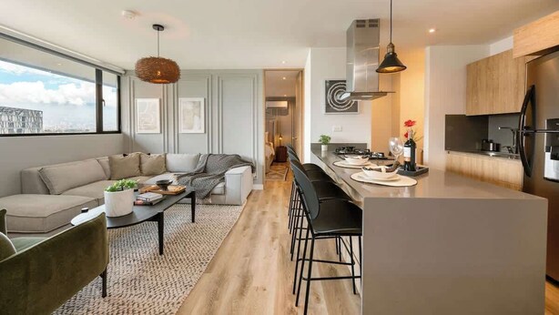Una cocina moderna con una isla central, una zona de comedor con sofá y vistas a través de un ventanal.