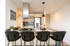 Une cuisine moderne avec un îlot central, des chaises noires et un luminaire suspendu.