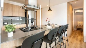 Una cocina moderna con una isla central, taburetes de bar, una lámpara colgante y vistas al exterior.