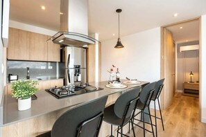 A modern kitchen with a central island, bar stools, a hanging pendant light, and a view of the outdoors.