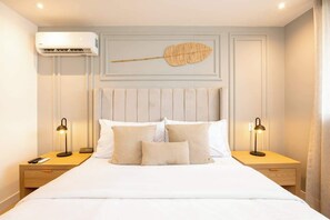 Une chambre d’hôtel avec un lit, deux tables de chevet, un appareil de climatisation et une feuille décorative accrochée au mur.