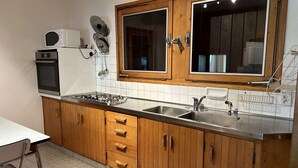 Een keuken met houten kastjes, een gasfornuis, een magnetron en een spoelbak.