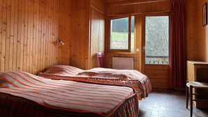 Een houten kamer met twee bedden, een radiator, een raam en een stoel.