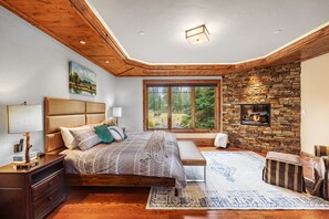 Una camera da letto con un letto grande, un camino in pietra, un soffitto in legno e una finestra che si affaccia sul verde.