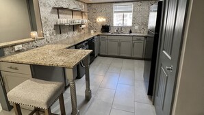A modern kitchen with a granite countertop, bar stools, a built-in oven, and a stainless steel refrigerator.